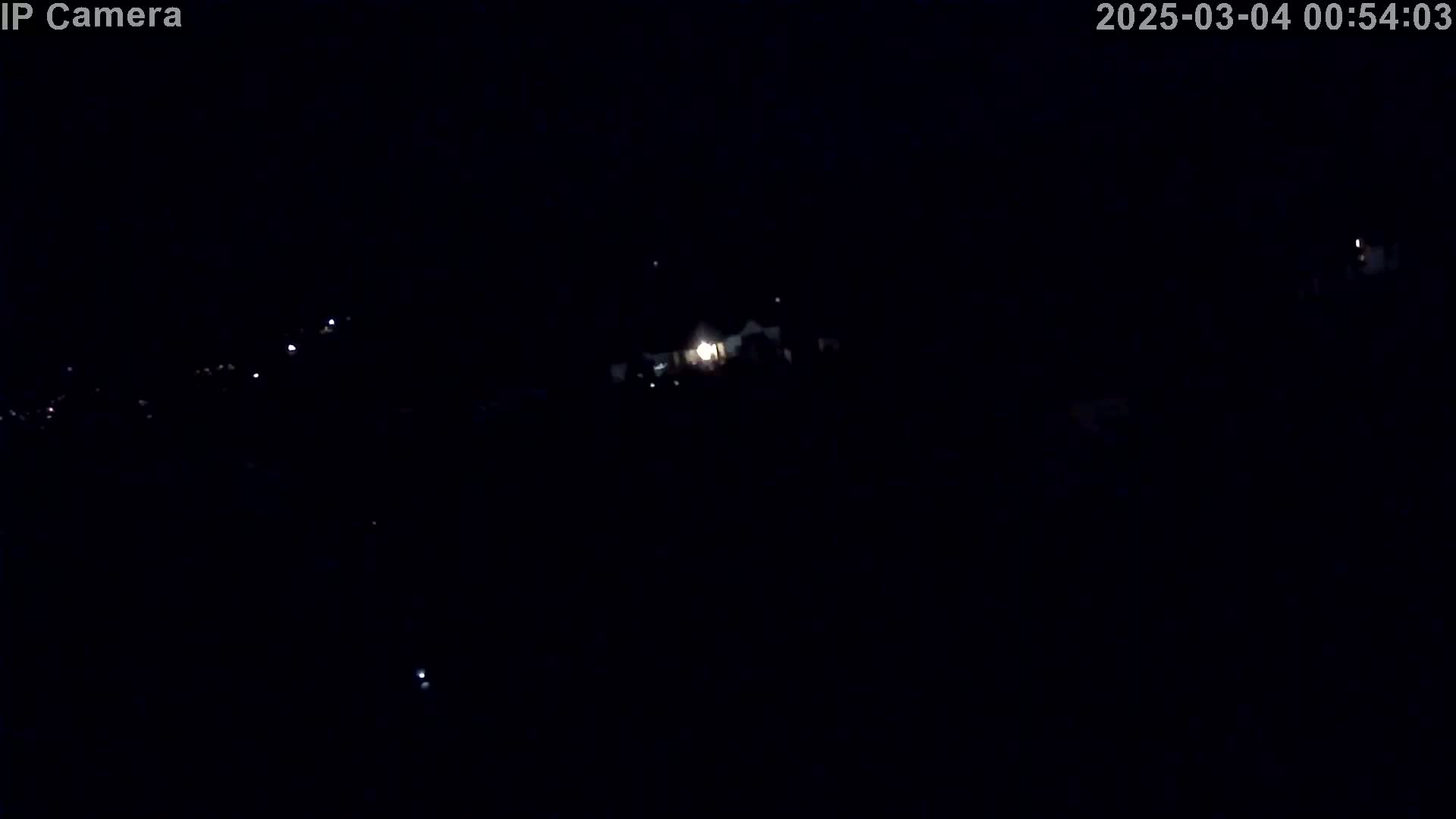 A dark, nighttime scene shows a few distant lights in the darkness.