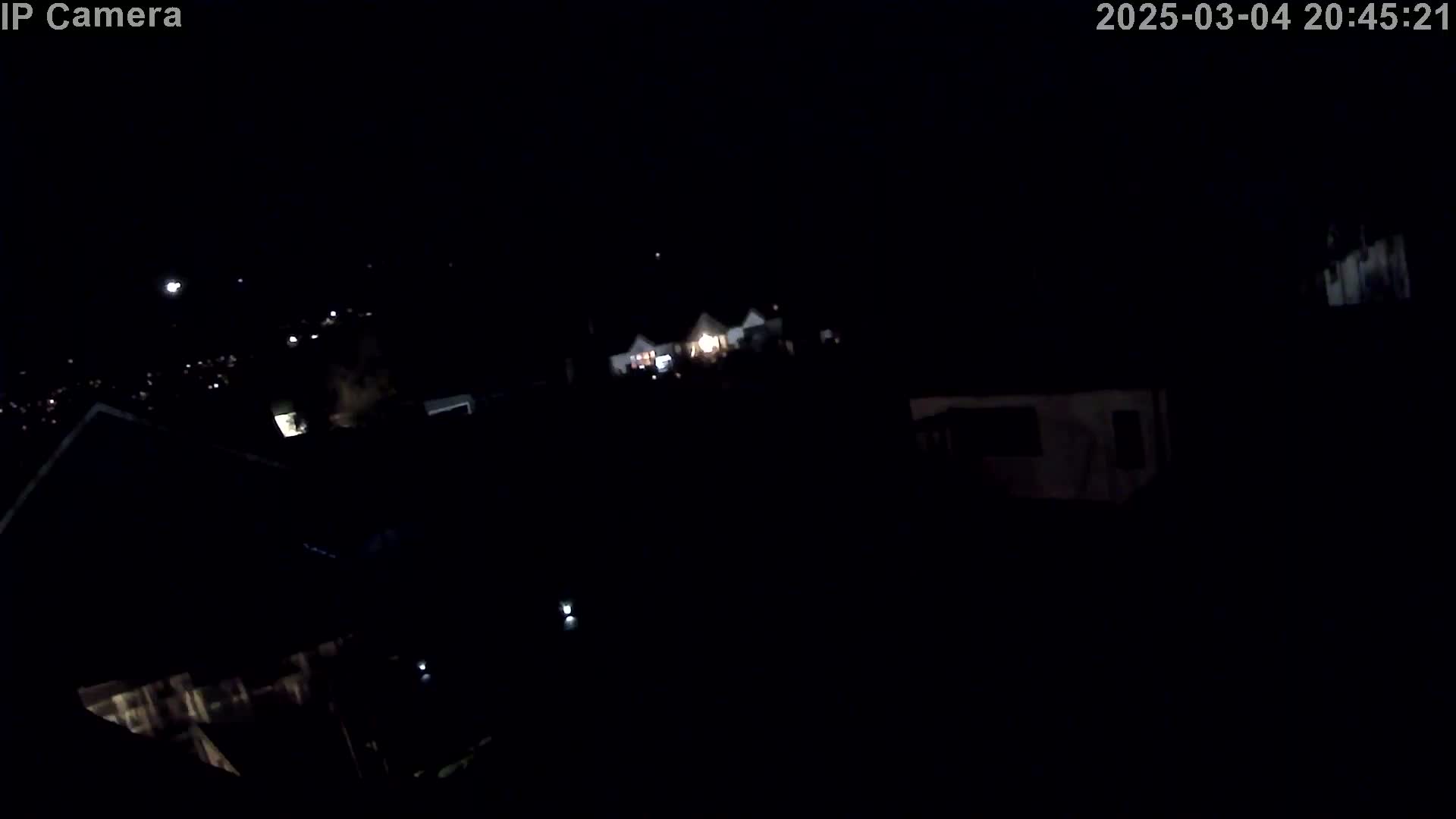 A nighttime, high-angle view shows dimly lit houses and a dark landscape under a clear, starless sky.