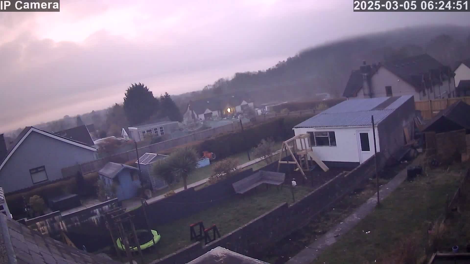 A backyard scene on a foggy morning shows houses and sheds, a trampoline, and a playset.