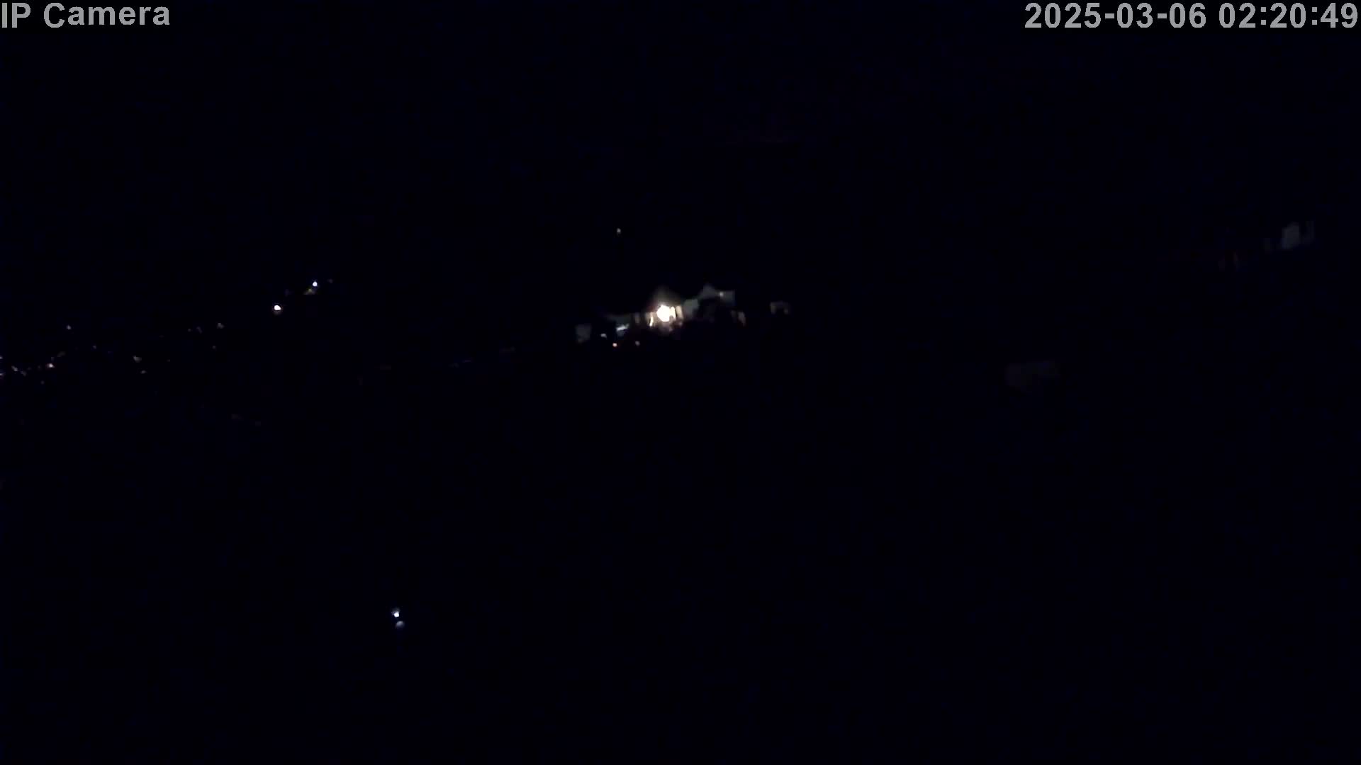 A dark, nighttime scene shows a few faint lights in the distance under a clear sky.