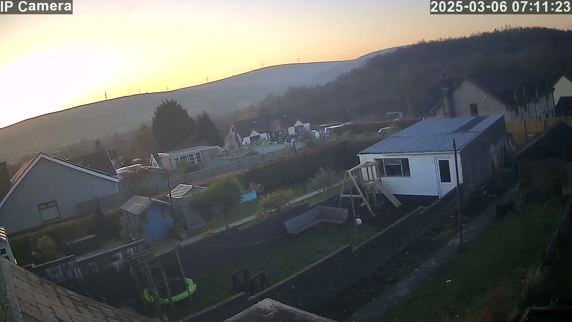 A residential backyard at sunrise overlooks a hazy valley with distant wind turbines.