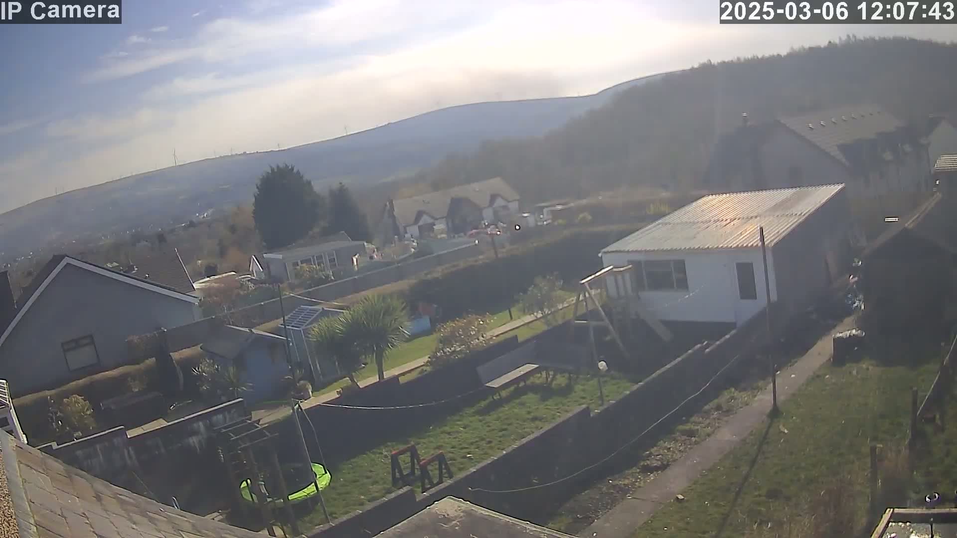 A hazy, sunny day overlooks a residential area with houses, gardens containing play structures, and a distant mountain range.