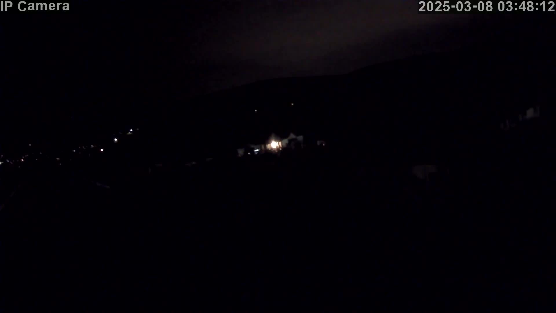 A nighttime, low-light view shows a dimly lit landscape with a few scattered points of light in the distance.