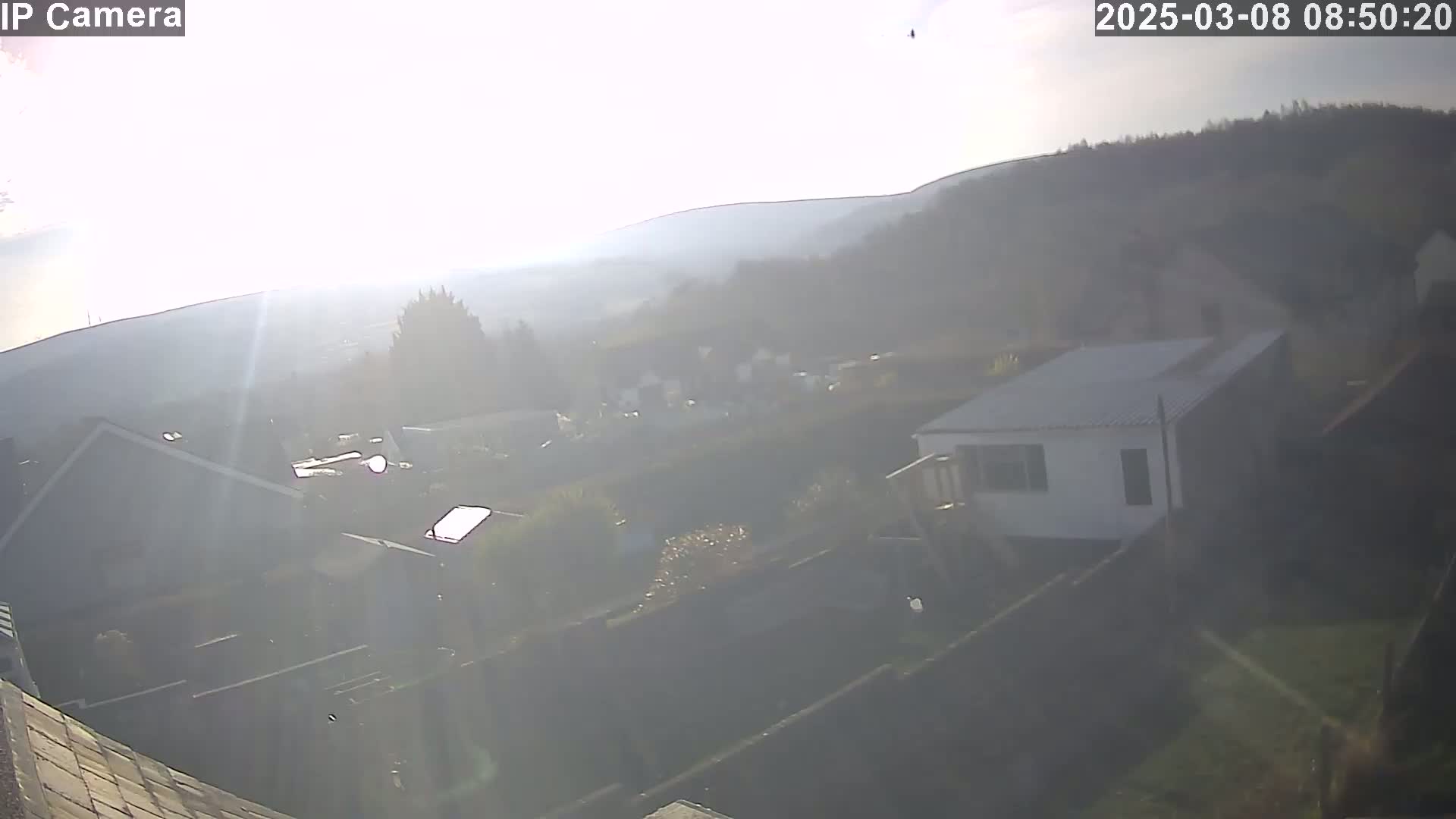 A hazy, sunlit view of a residential area with houses and hills in the background.