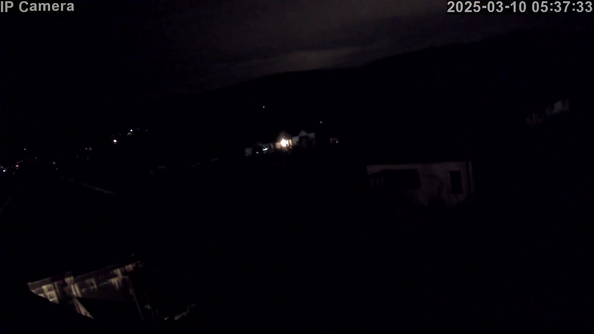 A nighttime, low-light view of a residential area, possibly under a partly cloudy sky.