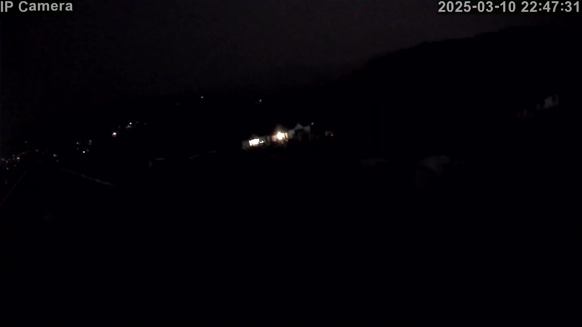 A nighttime, long-range view shows a few distant lights in a dark, hilly landscape.