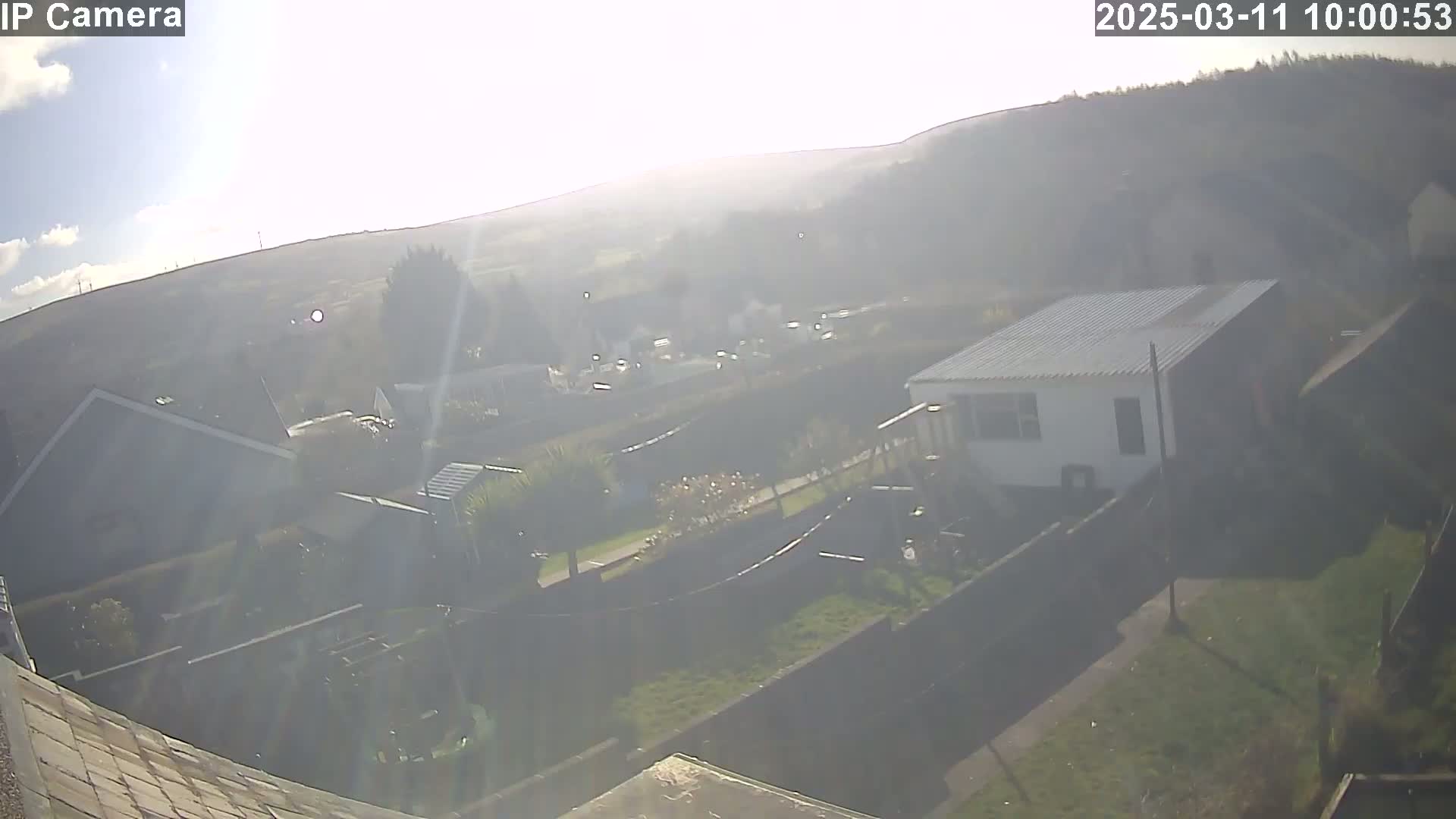 A hazy, sunny view overlooking a residential area with houses, gardens, and a hill in the background.