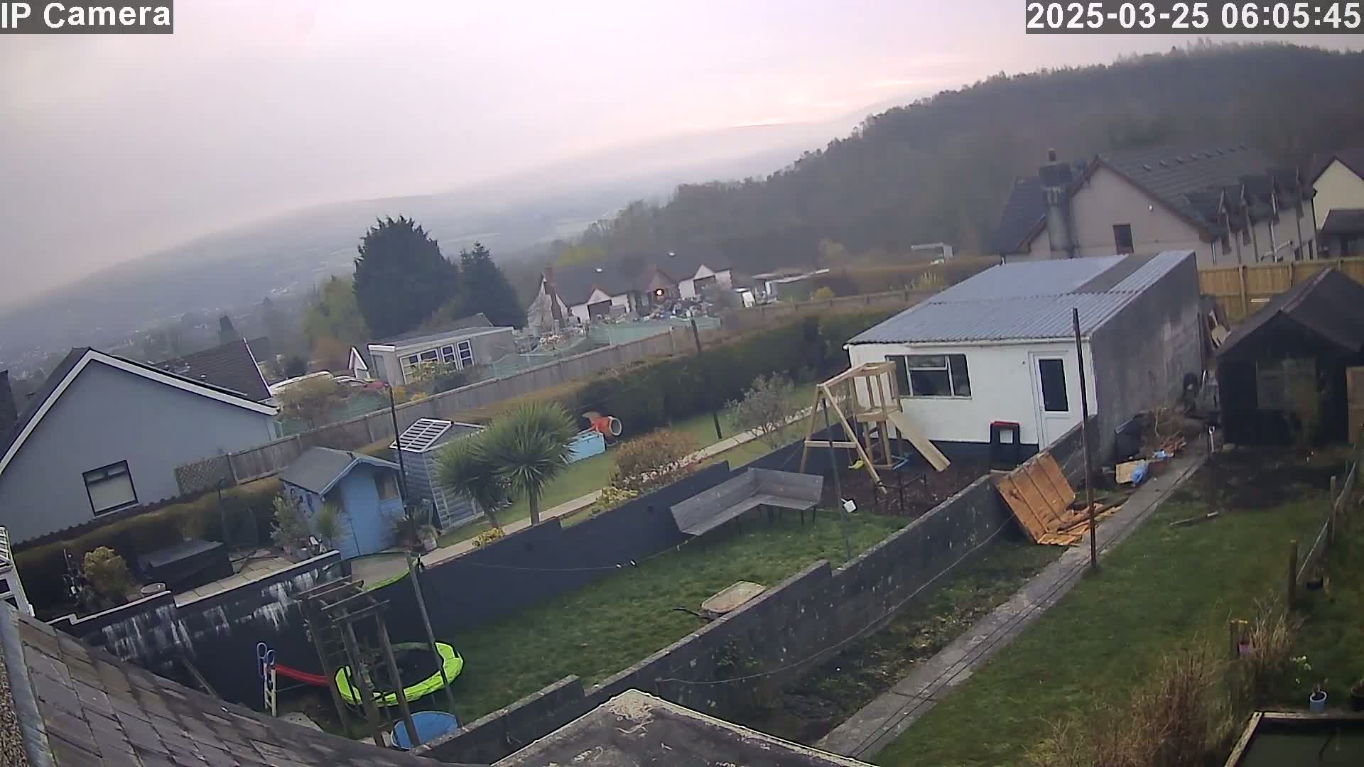 A backyard scene on an overcast day shows houses, sheds, a playset, and a trampoline, all overlooking a misty valley.