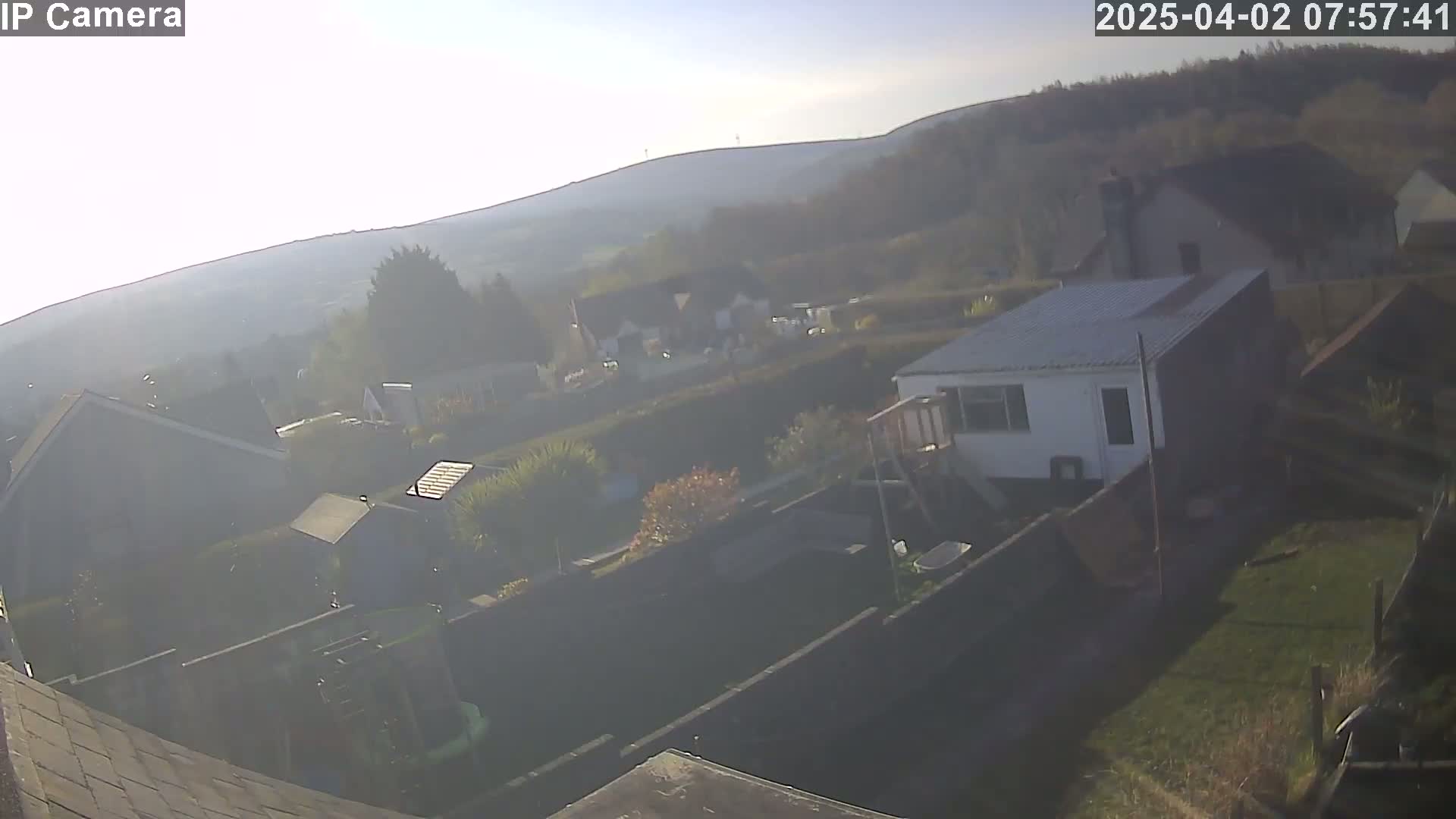 A hazy, sunlit view of houses and gardens, with hills visible in the background.