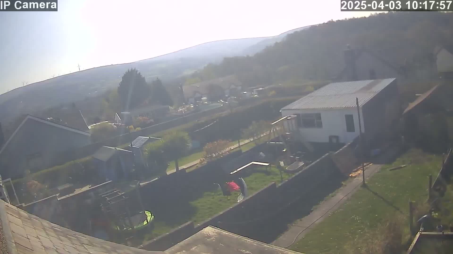A hazy, sunny day overlooks a residential backyard with a small shed, houses, and a grassy area containing children's play equipment.