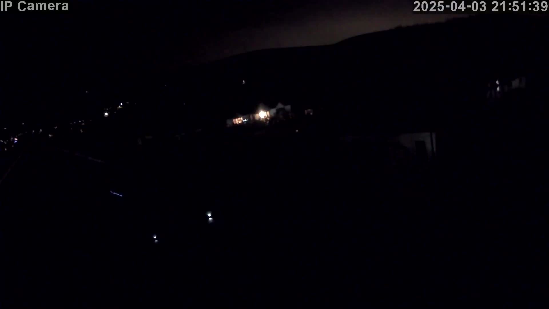 A nighttime, high-angle, long shot shows a dark landscape with sparsely scattered faint lights in the distance.