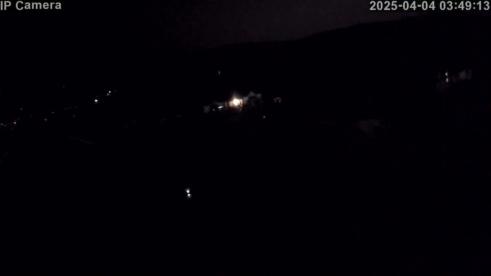 A nighttime, high-angle view shows a dark landscape with a few faint lights visible in the distance.