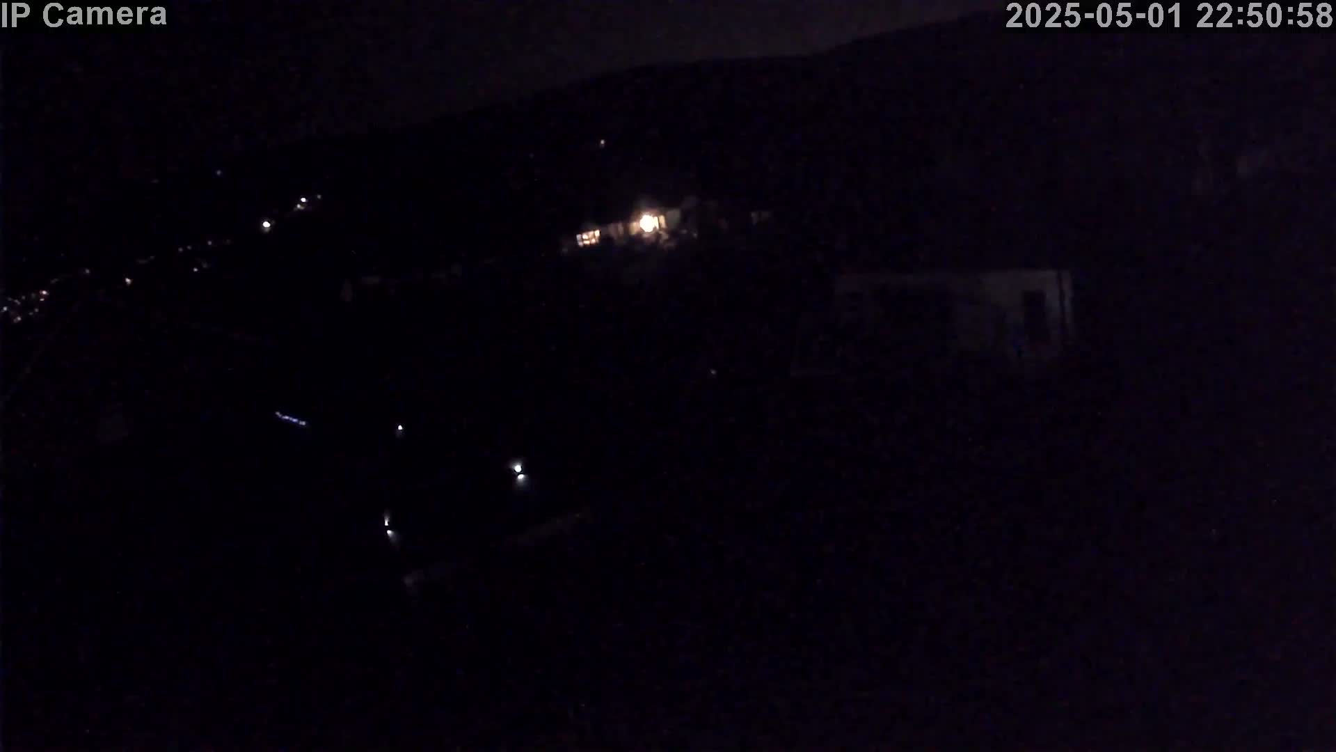 A nighttime, high-angle view shows dimly lit structures and a few scattered lights against a dark background.