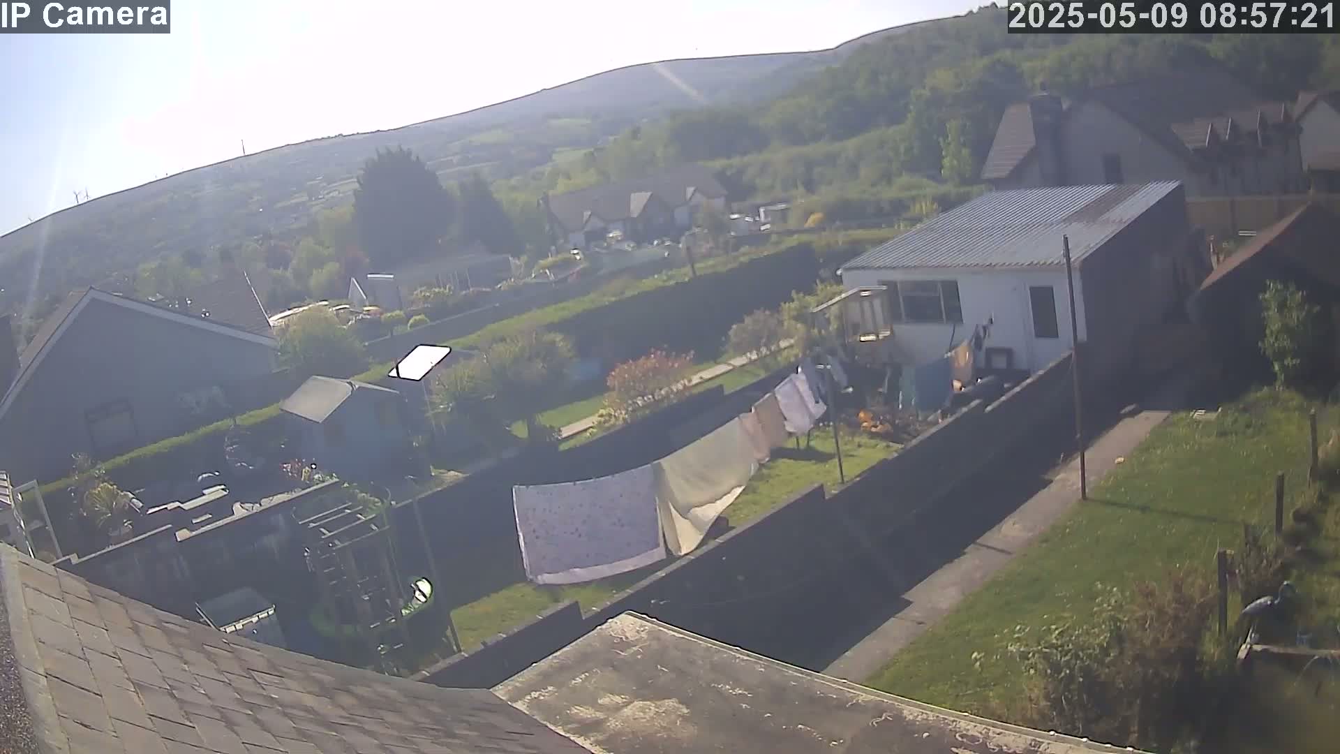 A high-angle, hazy view shows a backyard with a small shed, houses, and laundry drying in a sunny day.