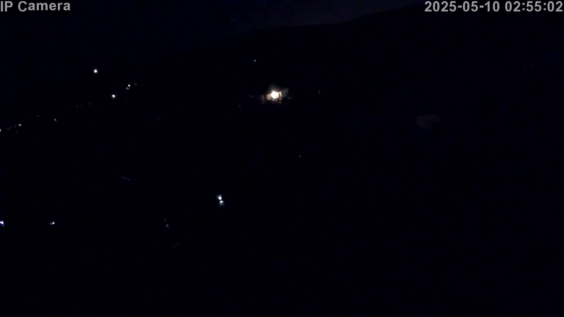 A nighttime, dark outdoor scene shows a few faint lights in the distance.