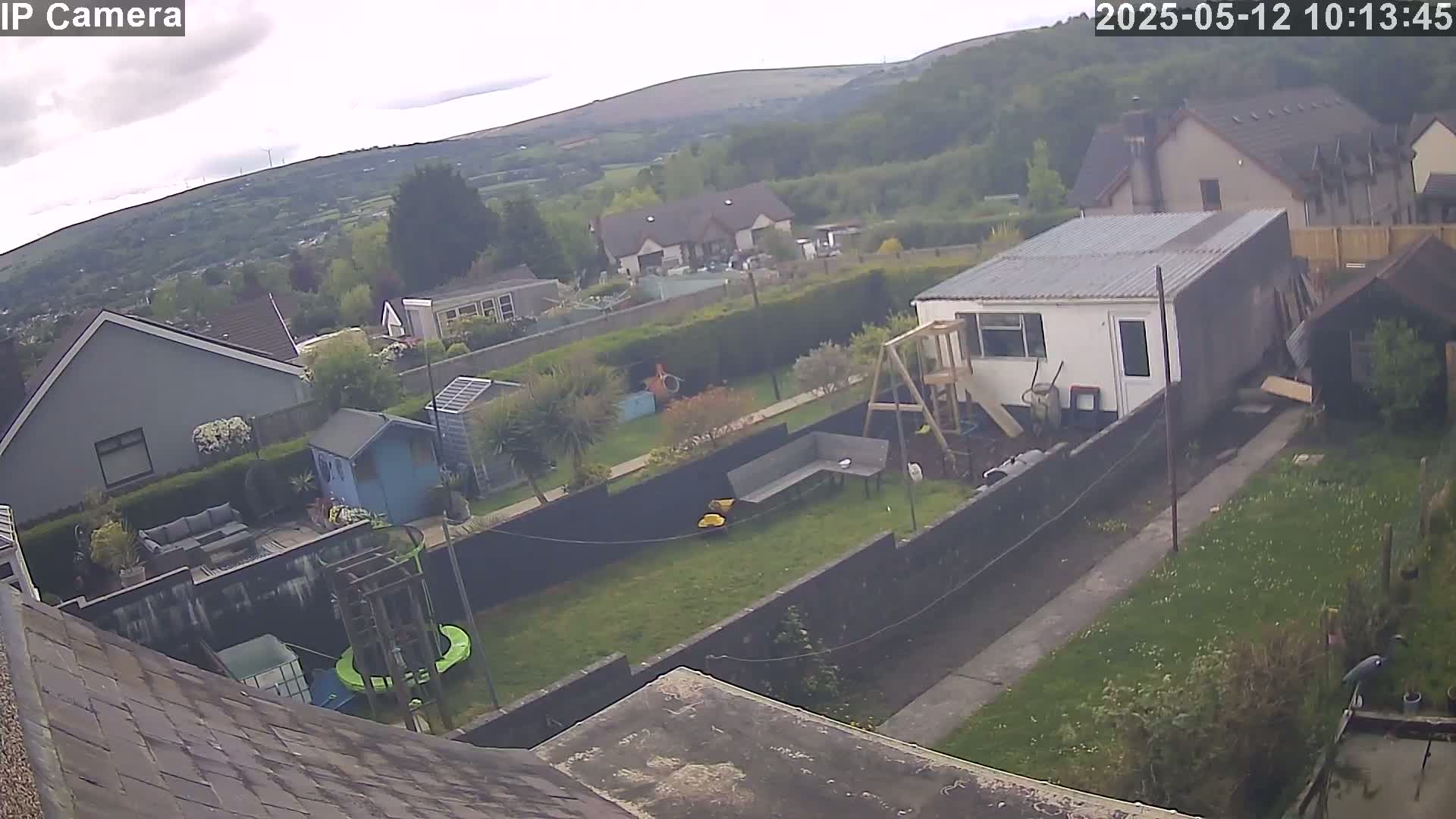 An overcast day reveals a backyard scene with houses and green hills in the distance, featuring a garden, playset, and small shed.