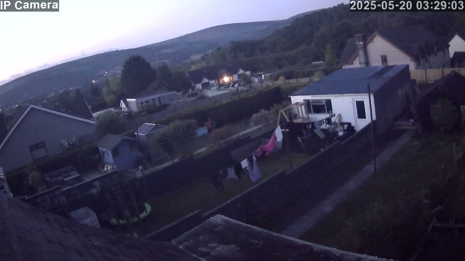 An aerial view at twilight shows several houses and gardens, with clothes hanging on a line in one backyard.