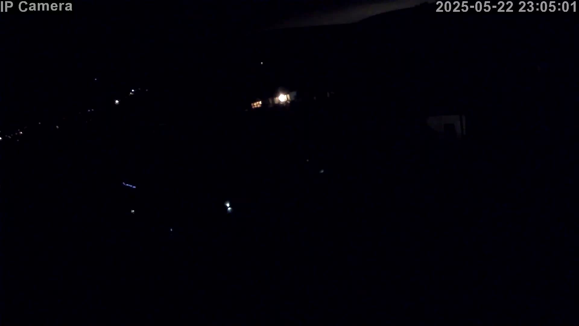 A nighttime, dark outdoor scene shows a few distant lights, possibly from buildings or vehicles, under a mostly clear sky.
