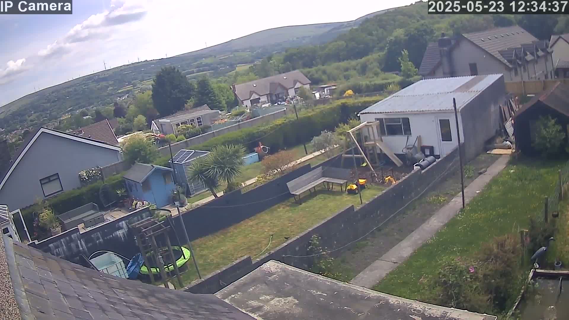 A backyard garden with houses and hills in the background under partly cloudy skies.