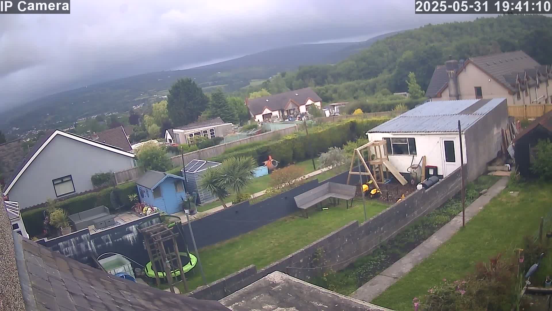 An overcast day shows a view of several houses and gardens, including a backyard with a shed, playground equipment, and a trampoline.