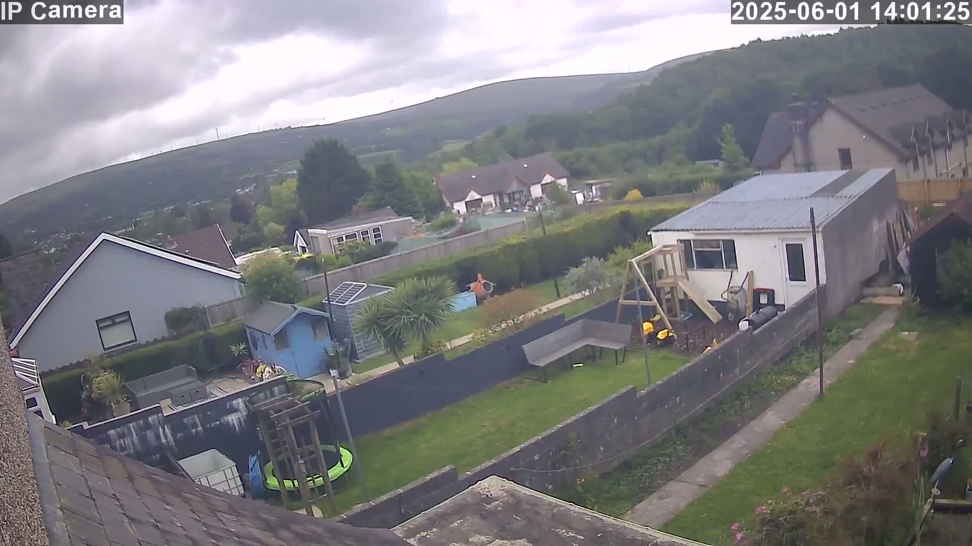 A backyard with houses and a hilly landscape in the background under an overcast sky.