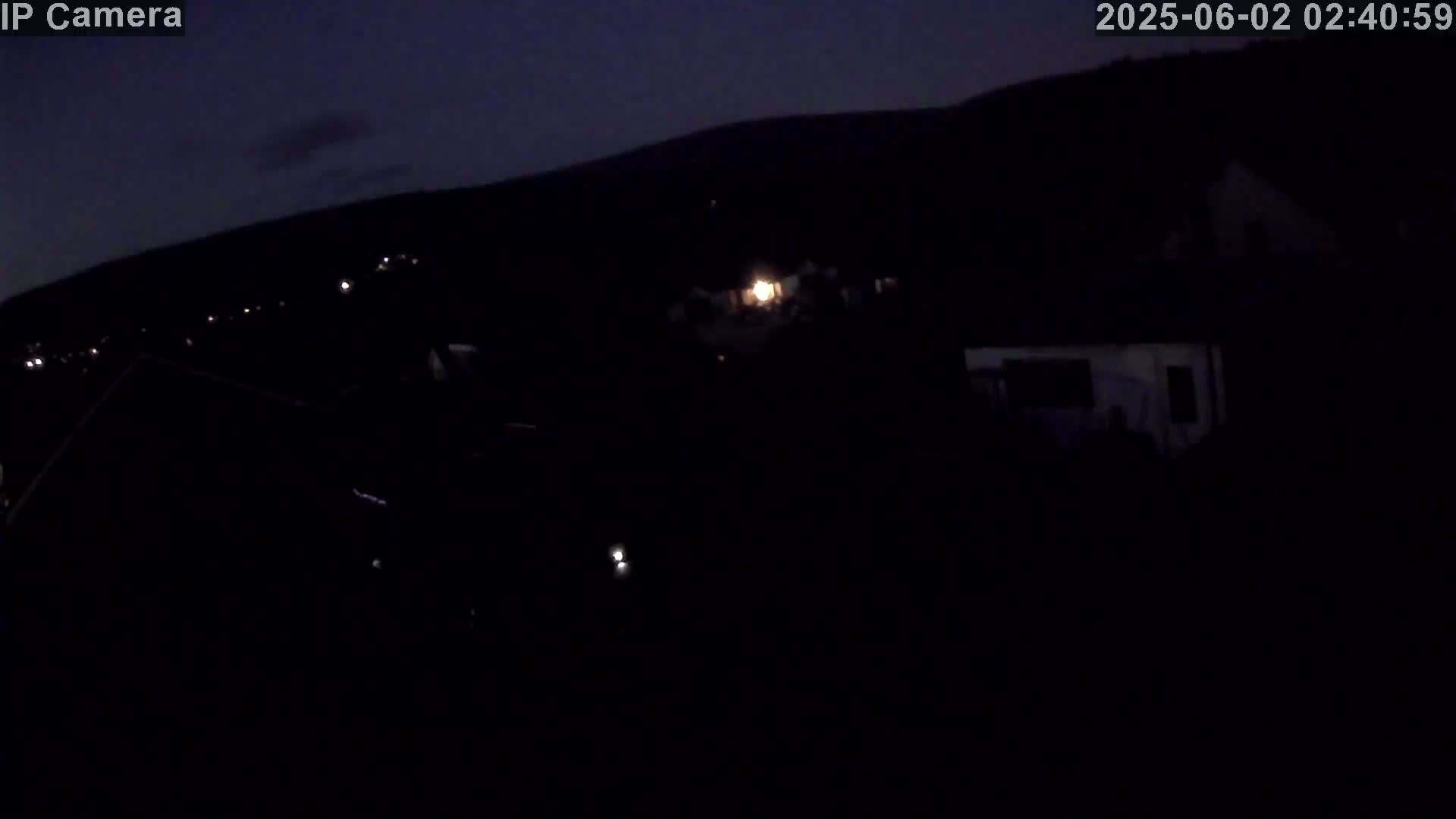 A dark, nighttime scene shows a few distant lights and buildings under a mostly clear, dark sky.