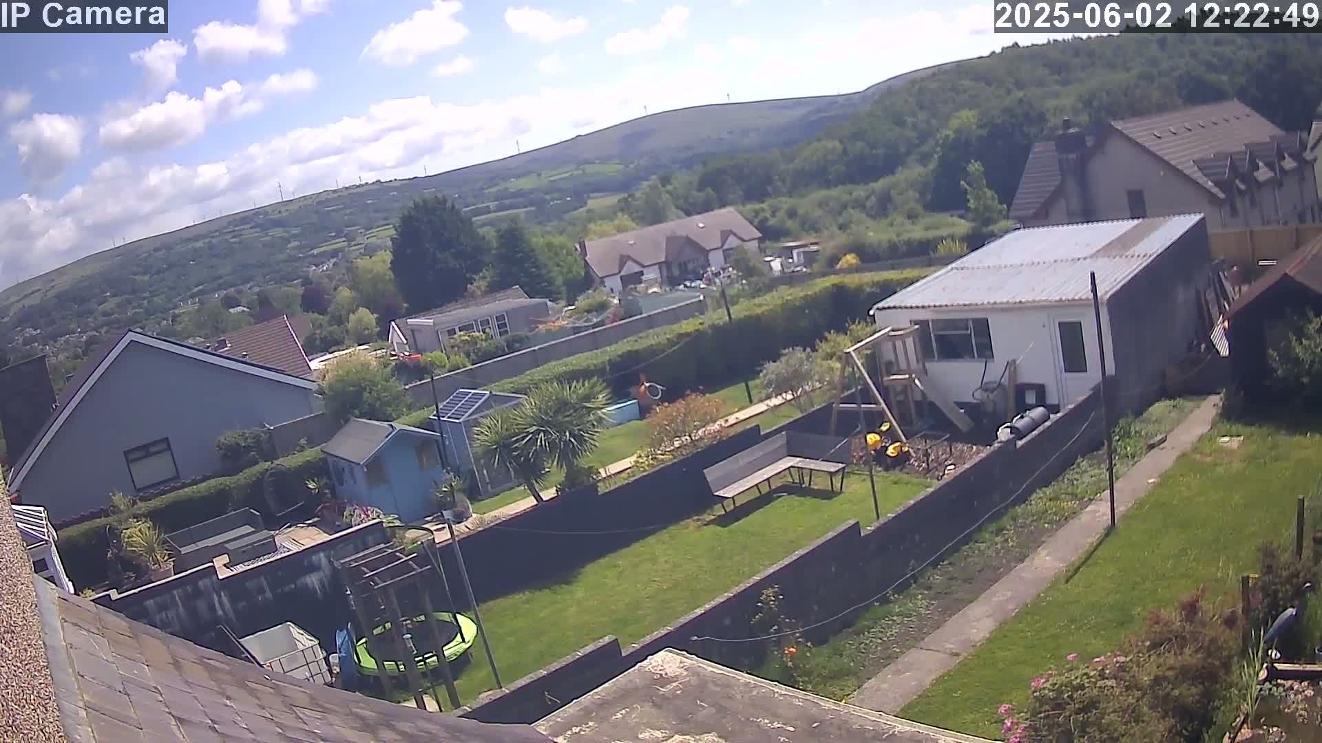 A backyard scene on a partly cloudy day features a garden, houses, and hills in the distance.
