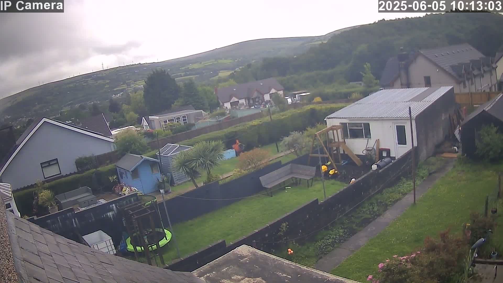 A backyard with houses and green hills in the background under an overcast sky.