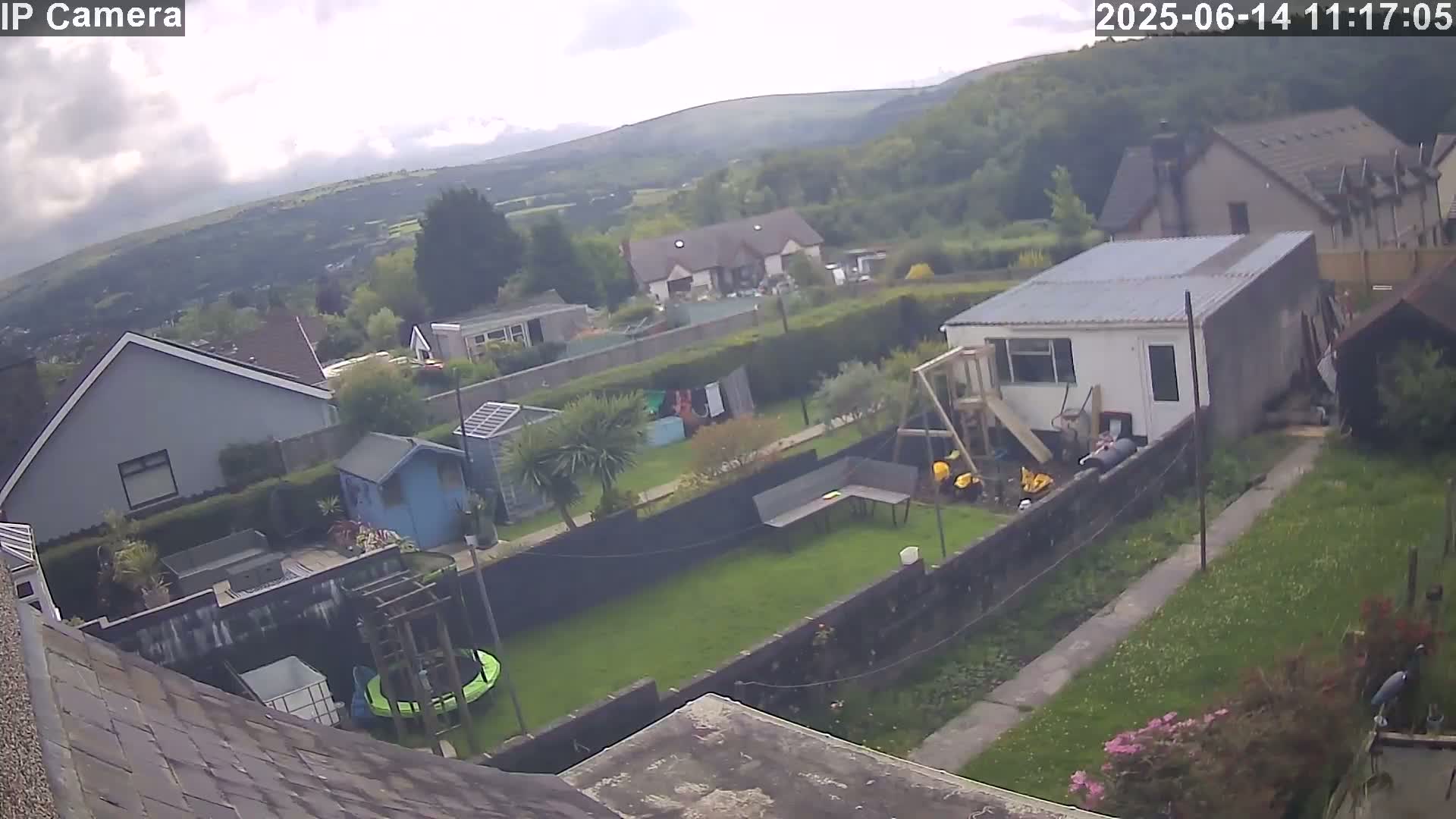 An overcast day reveals a backyard scene with houses and green spaces, including a trampoline and playset, overlooking a valley under a cloudy sky.