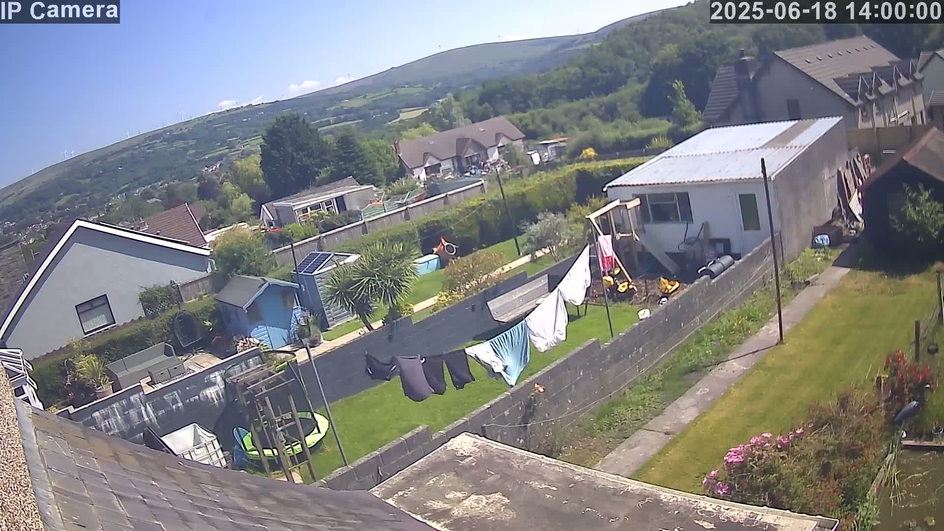 An aerial view of a residential backyard on a sunny day, showing houses, gardens, and laundry hanging on a clothesline.
