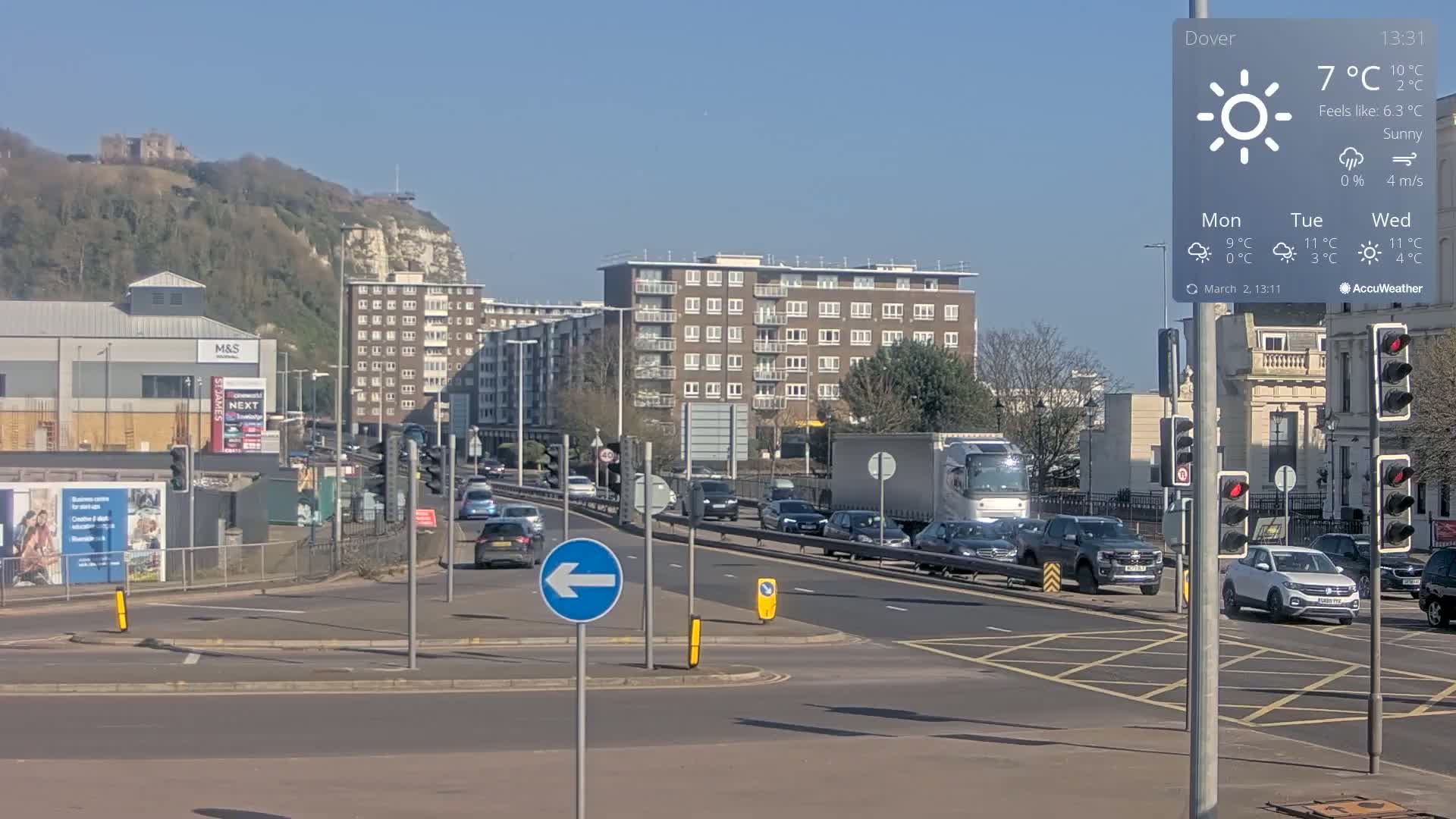 A sunny, 7°C day shows a multi-lane road intersection with traffic, buildings, and a distant hilltop castle in Dover.