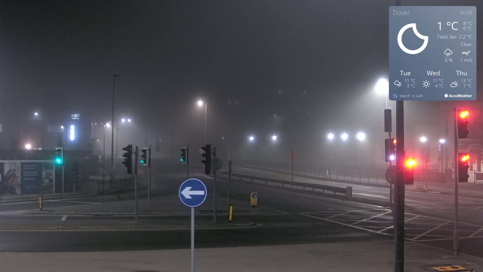 A foggy night scene shows a mostly empty intersection with traffic lights, streetlights, and a left-turn arrow sign.