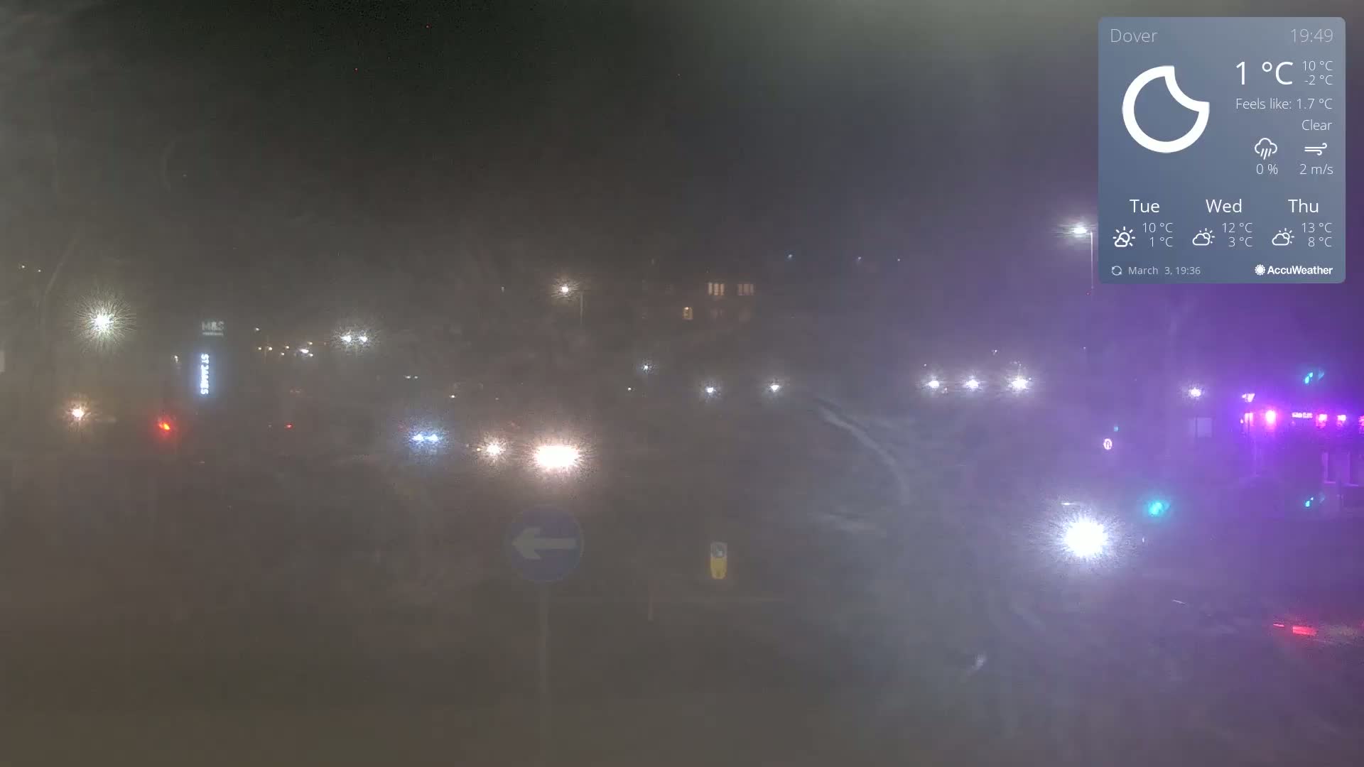 A hazy night scene shows a roadway with several vehicles and streetlights, under clear skies.