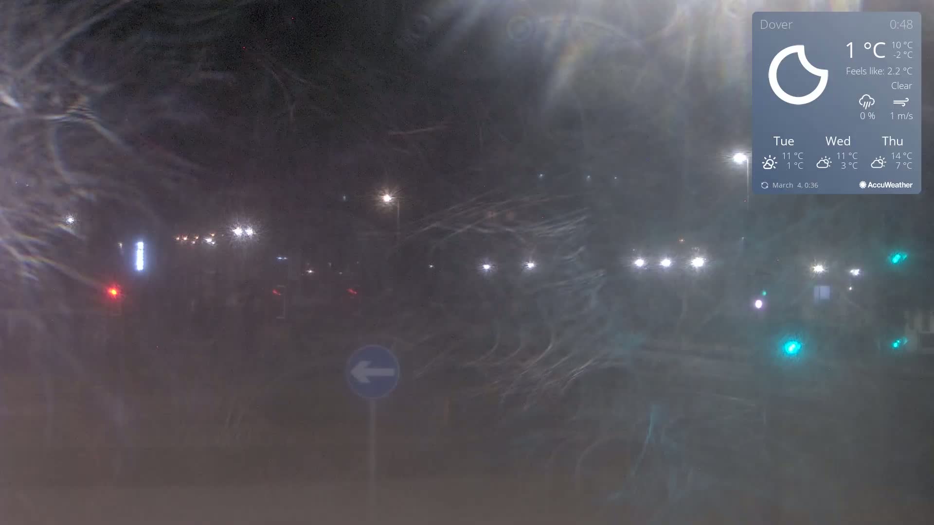 A night-time view of a road with streetlights, obscured by light fog or mist, under clear skies with a temperature of 1°C.