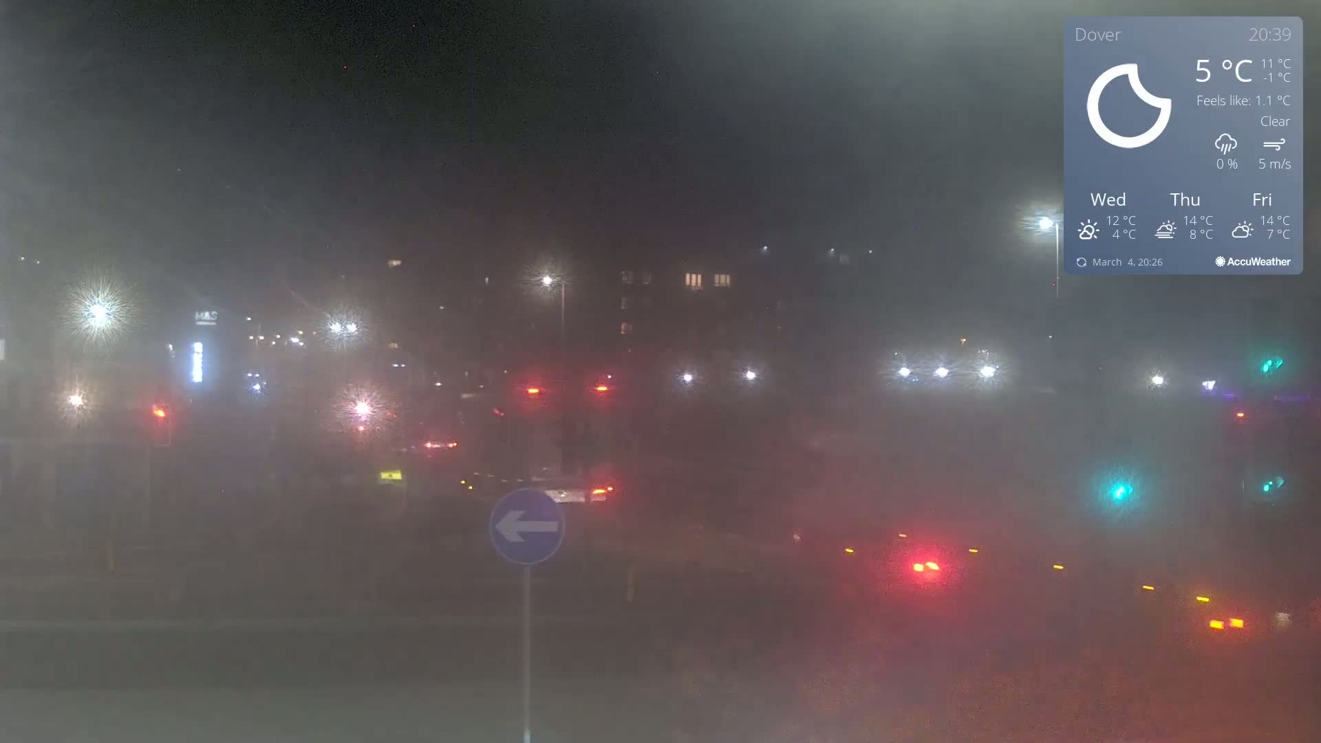 A foggy night scene shows a highway intersection with several vehicles' taillights visible in the distance.