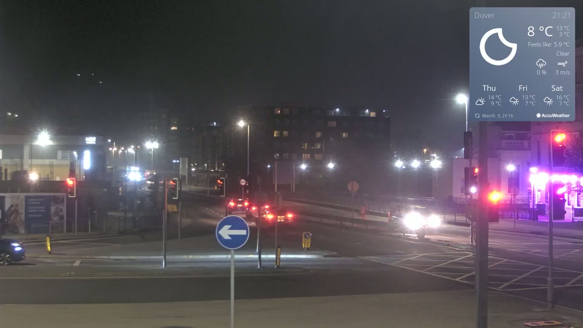 A nighttime view of a clear, sparsely trafficked intersection with streetlights illuminating several cars and buildings.