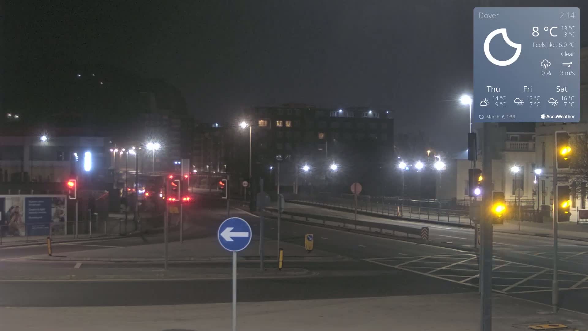 A nighttime, clear-weather view of a road intersection with traffic lights and several buildings in the background, illuminated by streetlights.