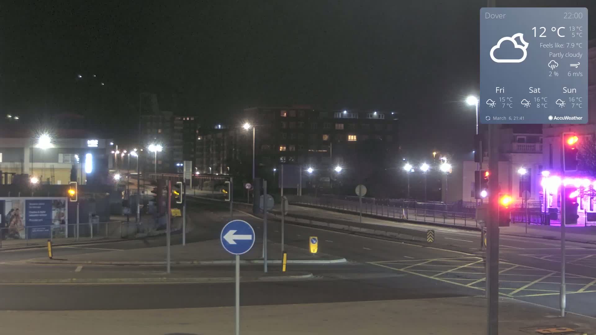 A mostly empty, well-lit road intersection at night under partly cloudy skies.