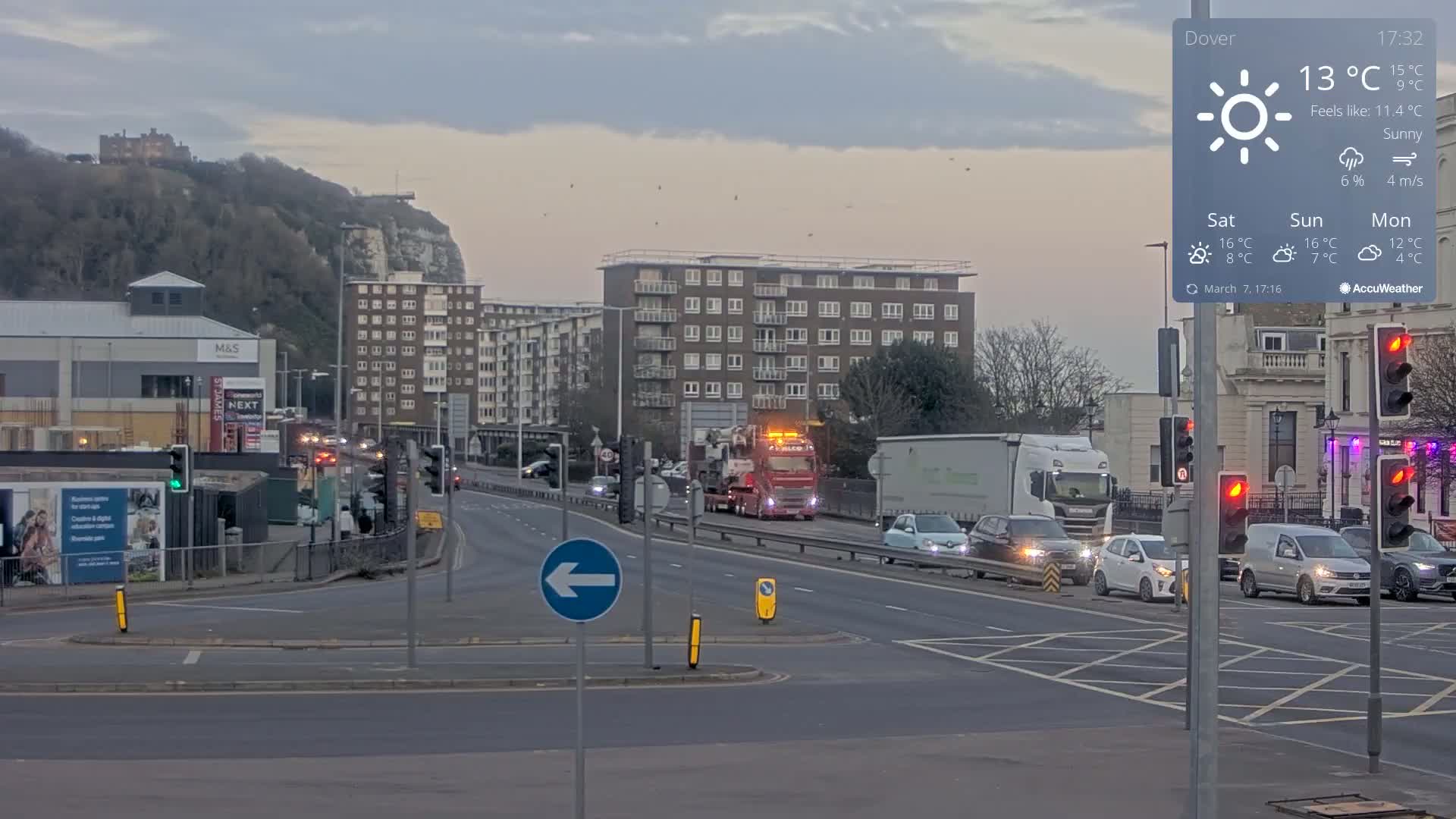 A sunny, but cool day shows traffic moving through a city intersection near a hill with a castle on top and several buildings in the background.
