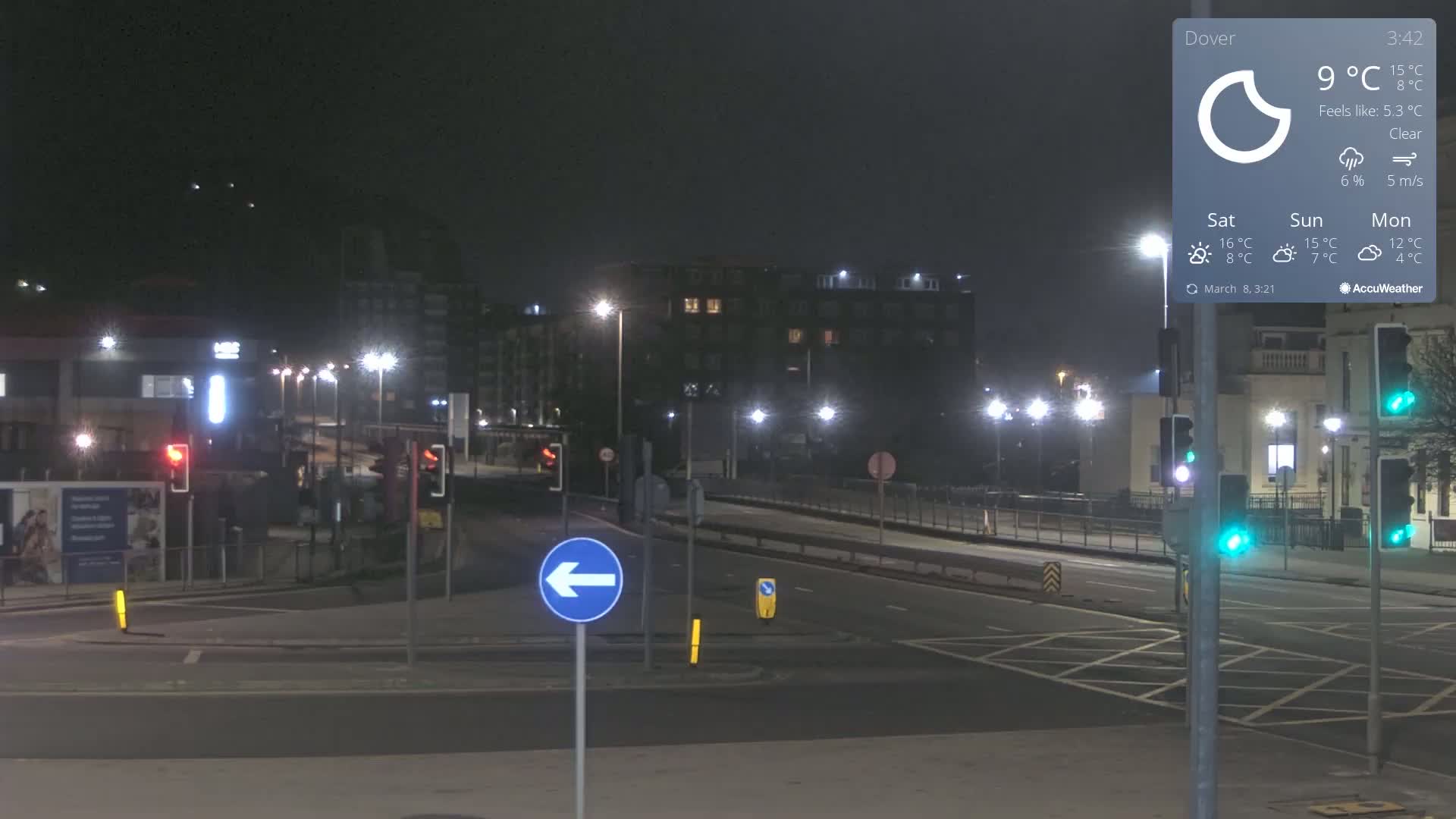 A nighttime, clear view of a mostly empty road intersection in a city, with buildings and streetlights visible.