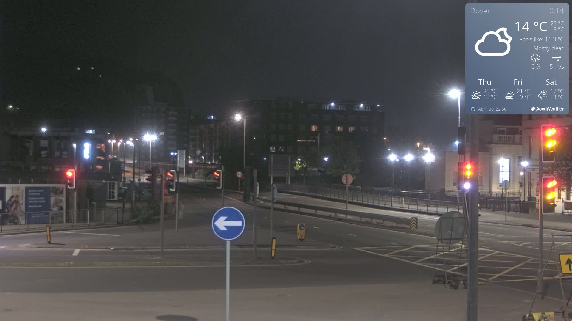 A mostly clear night scene shows a mostly empty intersection in a city with streetlights illuminating buildings and traffic signals.