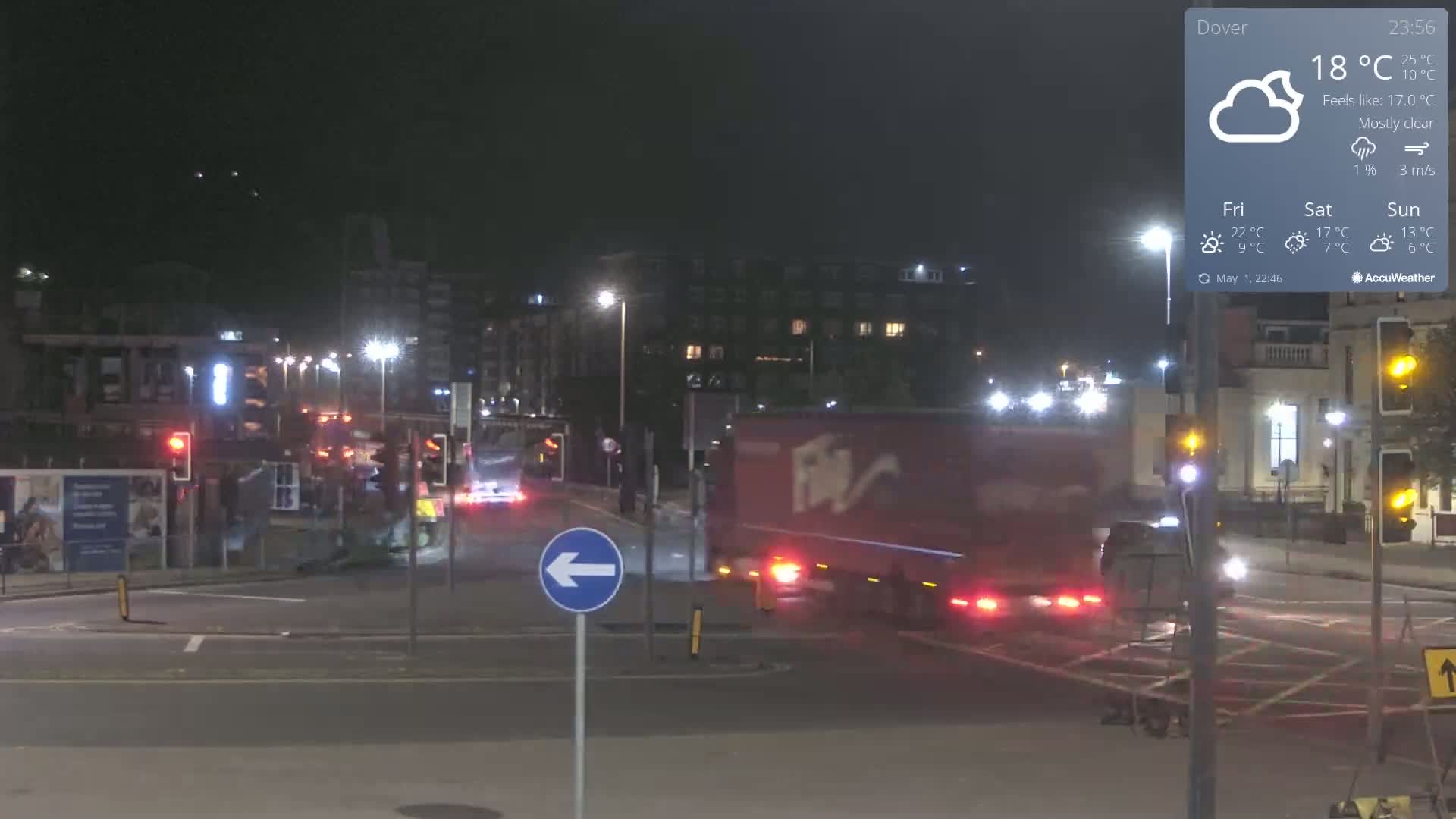 A mostly clear night scene shows a busy intersection with traffic lights and several vehicles, including a large red truck, under artificial street lighting.
