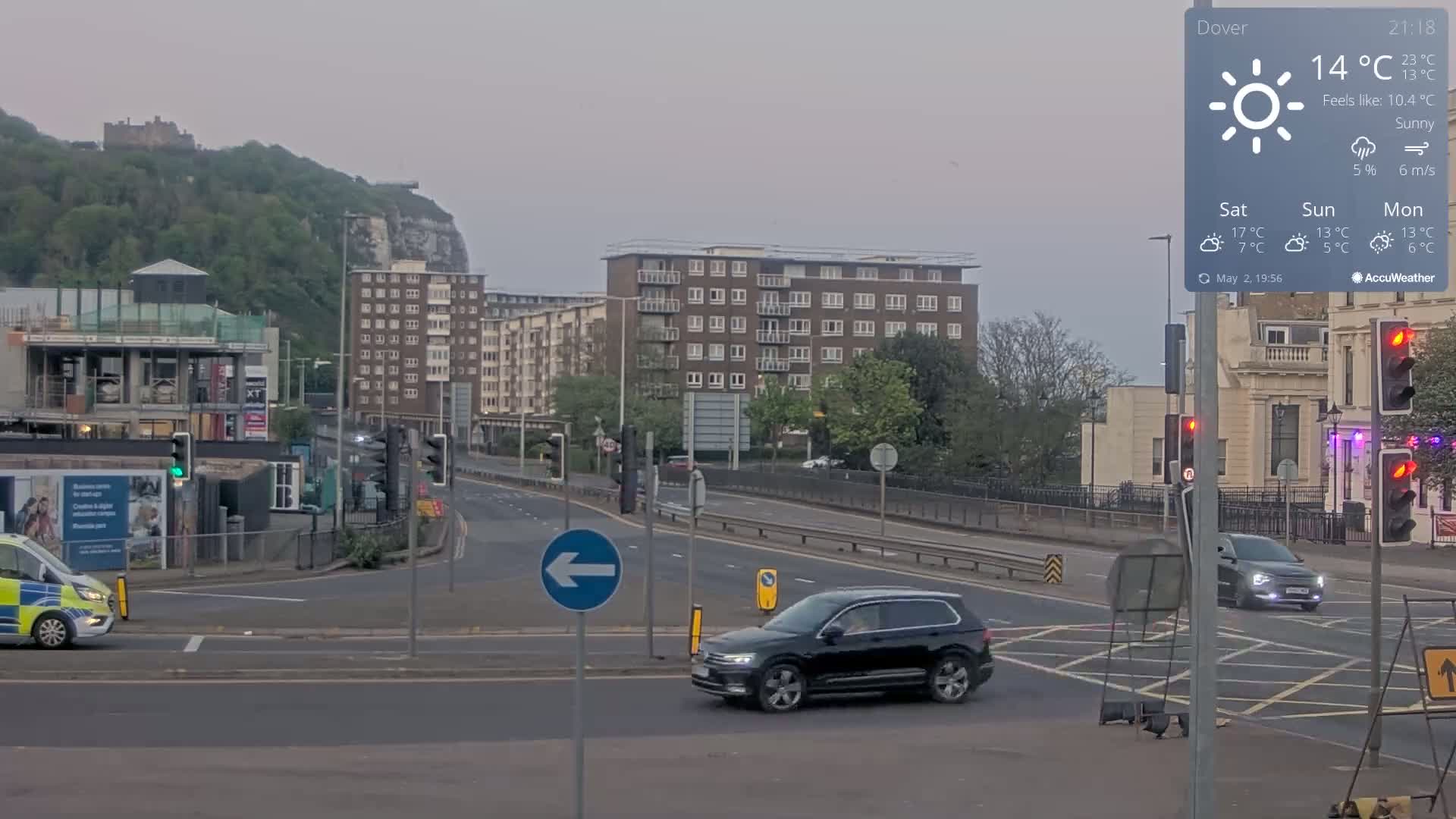 A sunny but cool day shows a street intersection with several vehicles, buildings, and a distant castle atop a hill.
