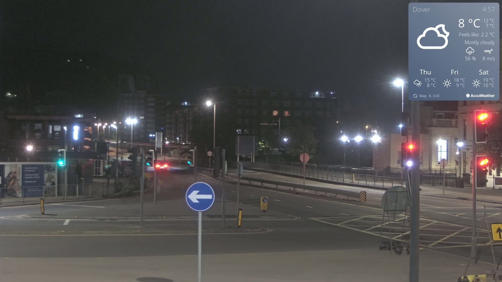 A mostly cloudy night scene shows a multi-lane road intersection with traffic lights and streetlights illuminating the area.