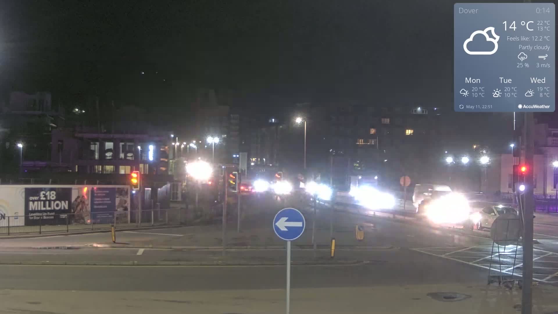 A nighttime, partly cloudy scene shows a multi-lane road intersection with moderate traffic flow under streetlights.