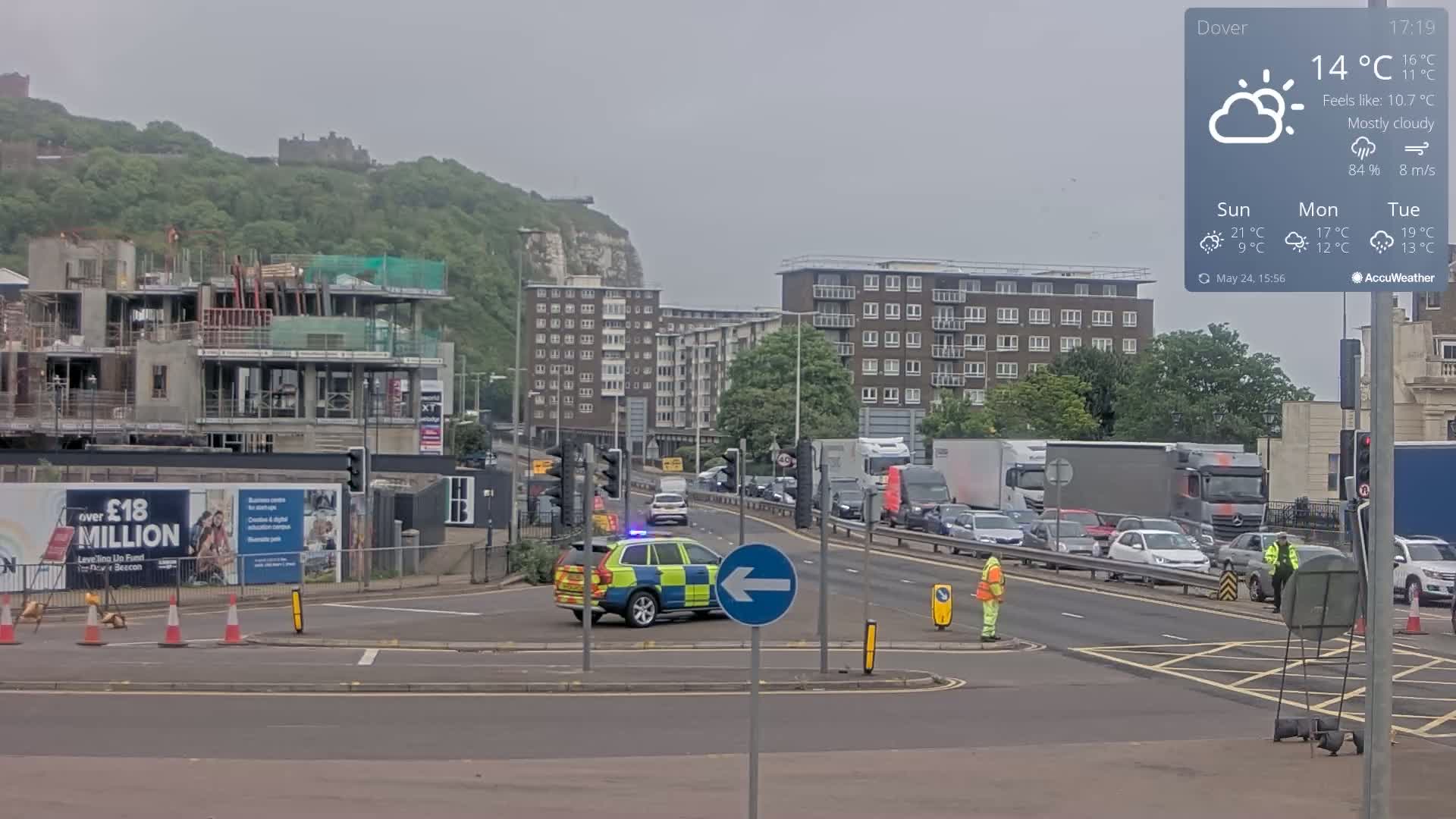 A police car is stopped at an intersection on a mostly cloudy day, with traffic congestion in the background, and a construction site visible beyond.