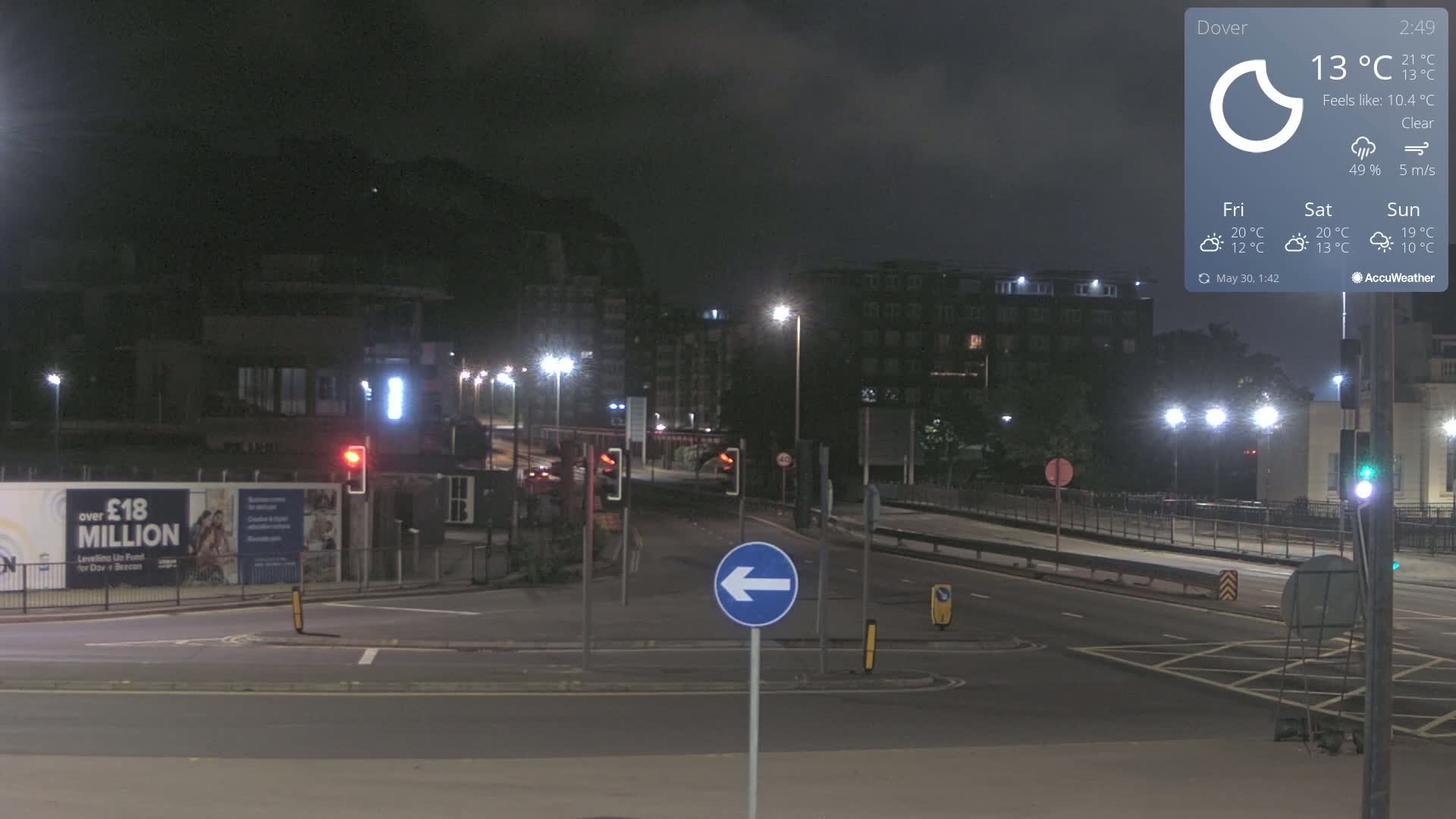 A nighttime view of a mostly empty intersection with streetlights illuminating buildings and a clear sky.