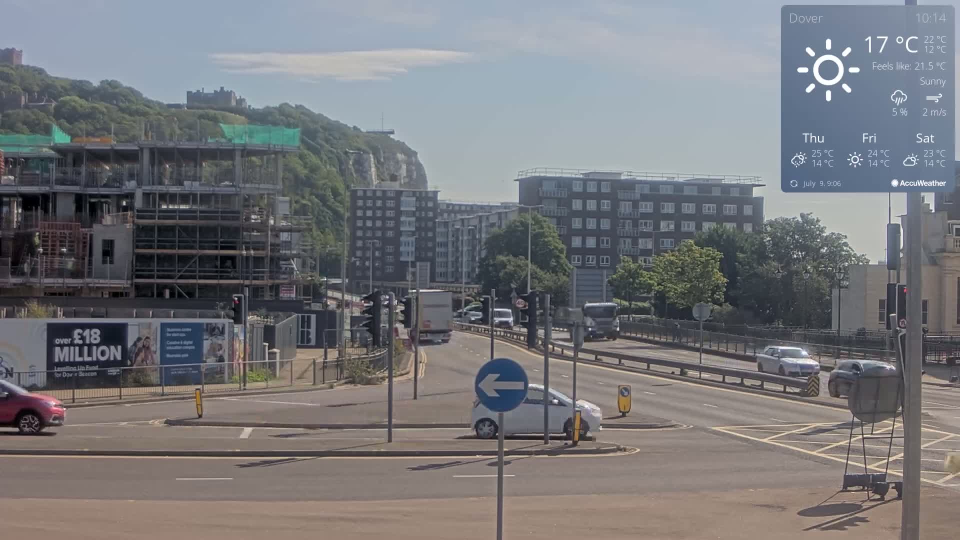 A sunny day reveals a busy road intersection with cars and a construction site, a backdrop of apartment buildings, and white cliffs in the distance.