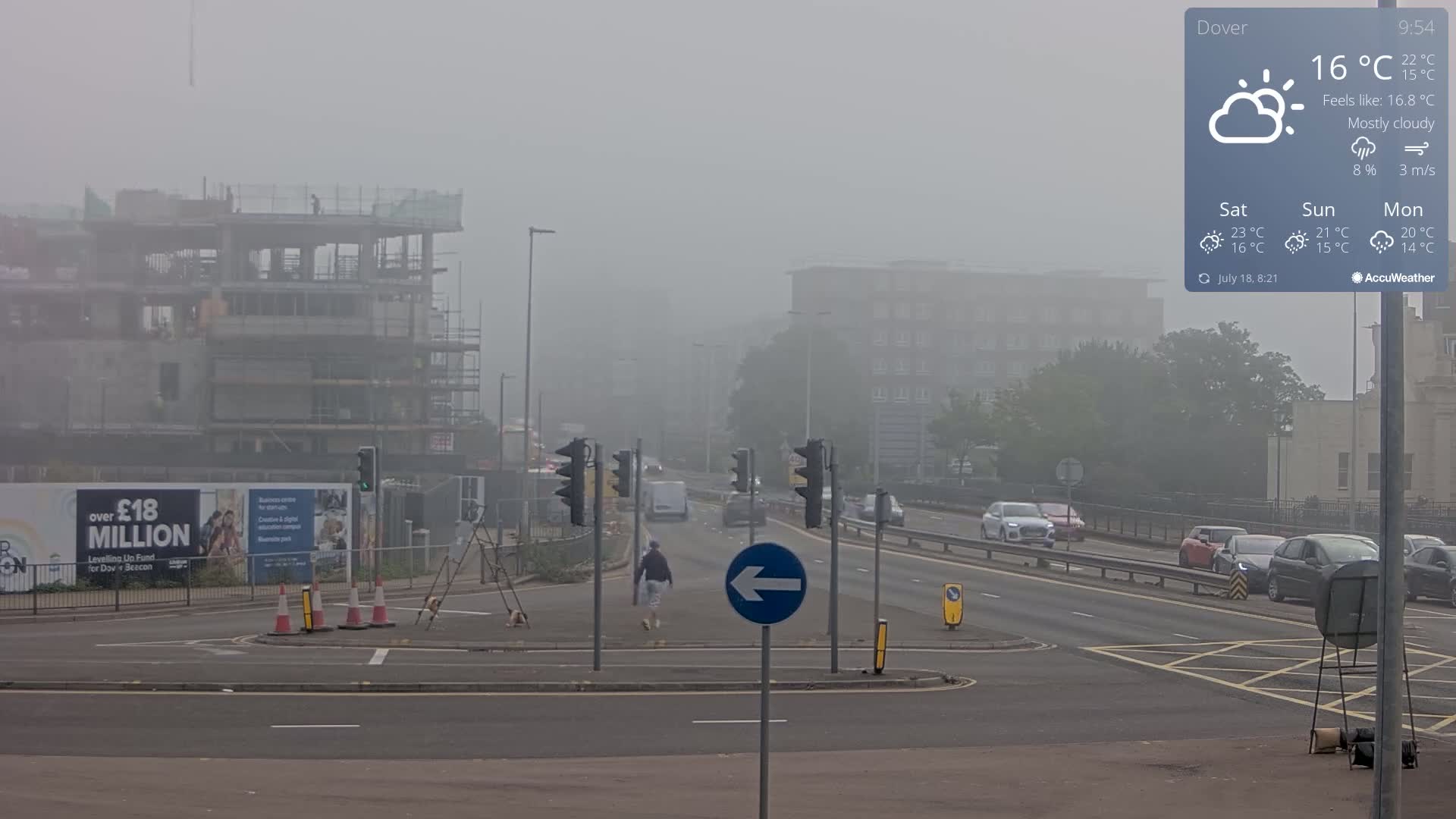 A mostly cloudy, foggy road scene shows a multi-lane road with cars and a pedestrian, alongside a partially constructed building and traffic lights.