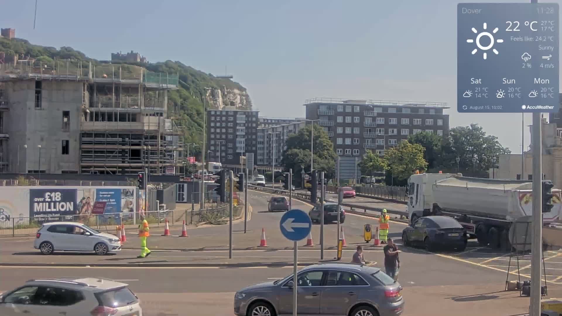 A mostly cloudy, foggy road scene shows a multi-lane road with cars and a pedestrian, alongside a partially constructed building and traffic lights.